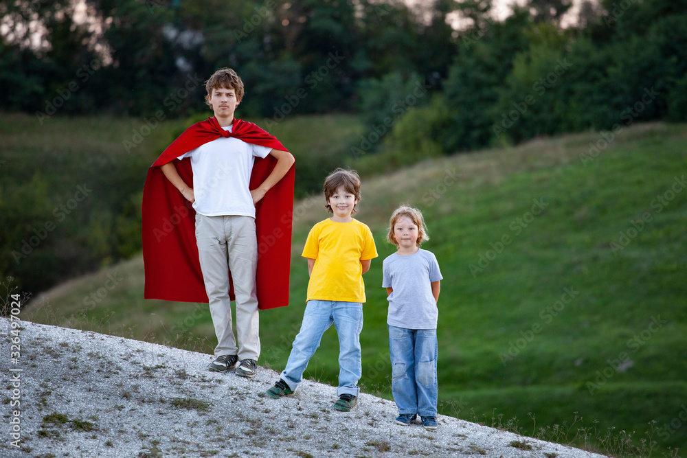 Boys playing superheroes outdoors, teenage superhero in a red cloak on a hill