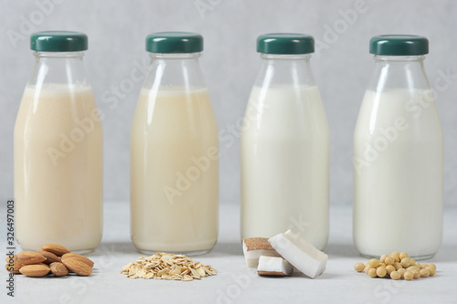 Concept alternative to cow's milk. Bottles with coconut, oat, soy and almond milk. Next to the bottles are pieces of coconut, almonds, oatmeal and soybeans. Light background. Close-up.