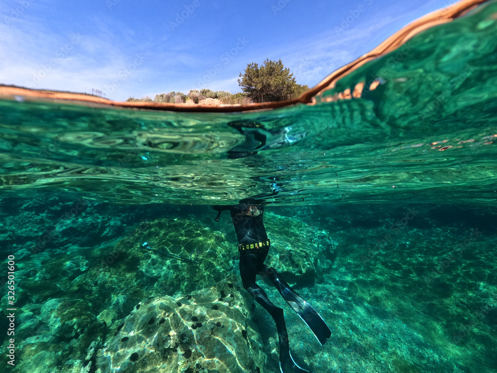 Underwater above and below photo of spear fishing diver in deep emerald exotic paradise bay with caves and rocky seascape