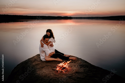 Young couple embracing and kissing on Sunset coast near the fire. Romantic love story.