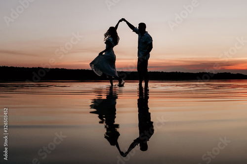 Young couple dancing in the water on Sunset. Two silhouettes against the sun. Romantic love story.