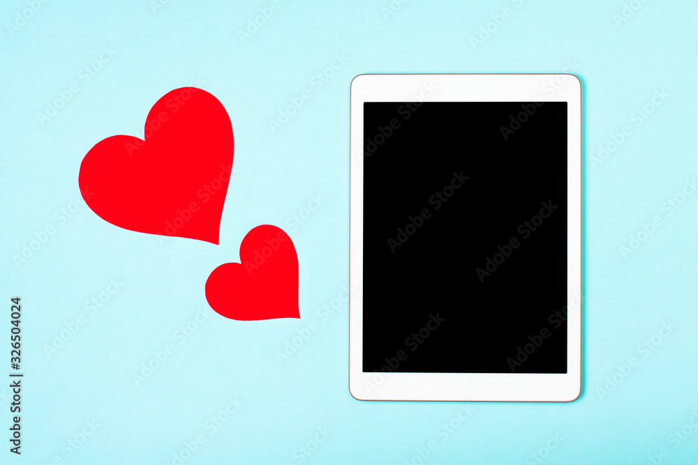 Tablet on a blue background with cute hearts. The concept of meeting website, love in internet, love to your gadget and technology, love correspondence, Valentine's Day, surprise. Flat lay Tablet on a blue background with cute hearts. The concept of meeting website, love in internet, love to your gadget and technology, love correspondence, Valentine's Day, surprise. Flat lay