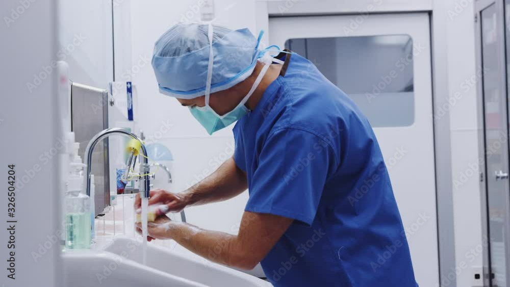 Male Surgeon Wearing Scrubs Washing Hands Before Operation In Hospital Operating Theater Male Surgeon Wearing Scrubs Washing Hands Before Operation In Hospital Operating Theater