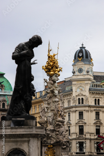 Monument of the Tower of the plague of Vienna between a bronze statue and a beautiful tower of a typical building, Austria.