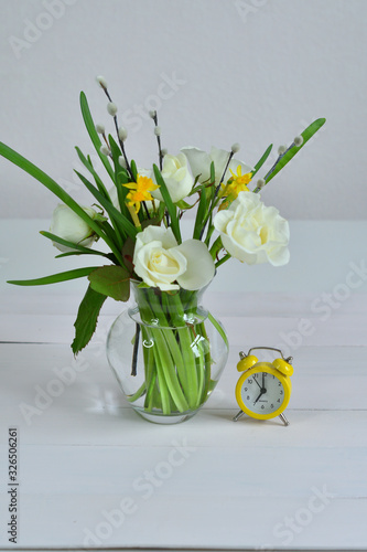 Glass vaza with a bouquet of spring flowers and yellow alarm clock .Bunch of pussy willow branches with catkins and white roses.Spring card for Mother's Day, Women's Day. copy space. photo