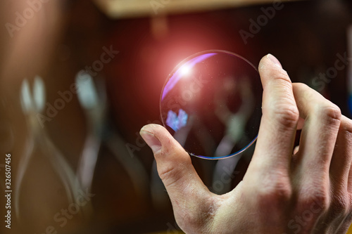 ophthalmologist hands showing a glass lens for spectacles. Blurred background. Ophtalmologist equipment. Vision correction concept. Closeup photo