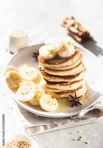 Pancakes with banana, honey and nuts on ceramic plate, sunny shadowed table surface. Natural light and shadows food photography concept. Breakfast.