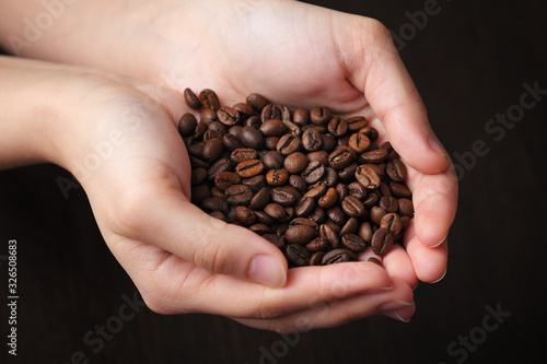 coffee beans in female hands on dark textured background