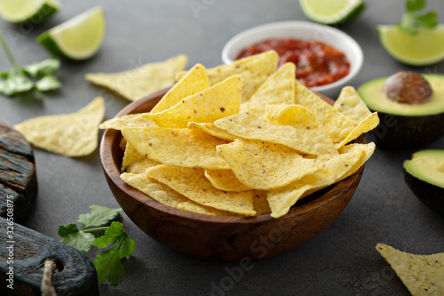 Tortilla chips in a bowl with salsa, limes and avocados photo