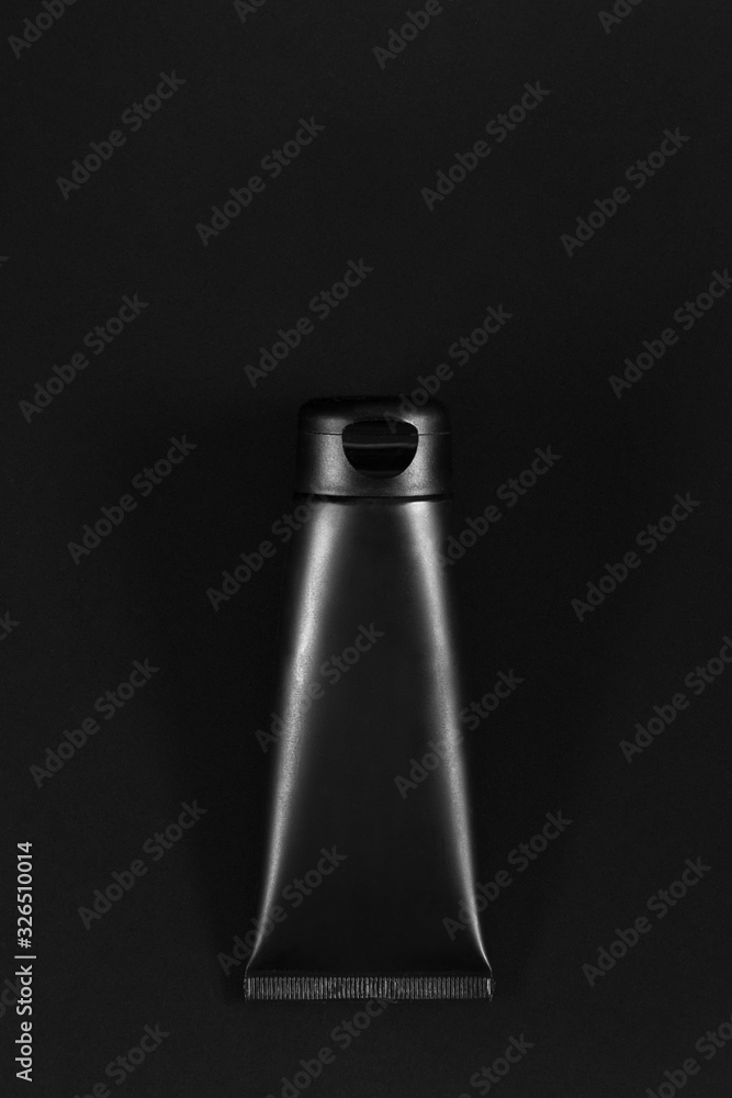 Black cream tube on black table. Royal product. Empty place for logo on tube. Directly above lowkey flat lay. Black cream tube on black table. Royal product. Empty place for logo on tube. Directly above lowkey flat lay.