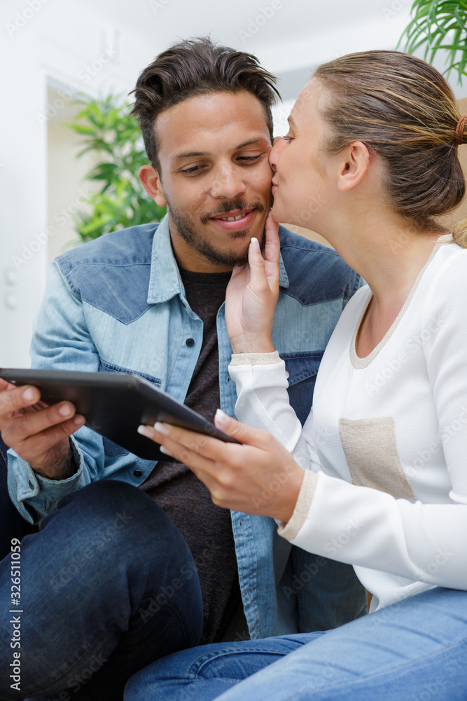 happy wife kissing her husband whos holding a tablet