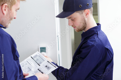 engineer and apprentice adjusting thermostat for efficient automated heating system photo