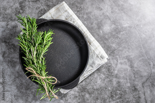 Empty black pan with rosemary twigs and napkin on dark stone background. Table setting. Restaurant menu template.
