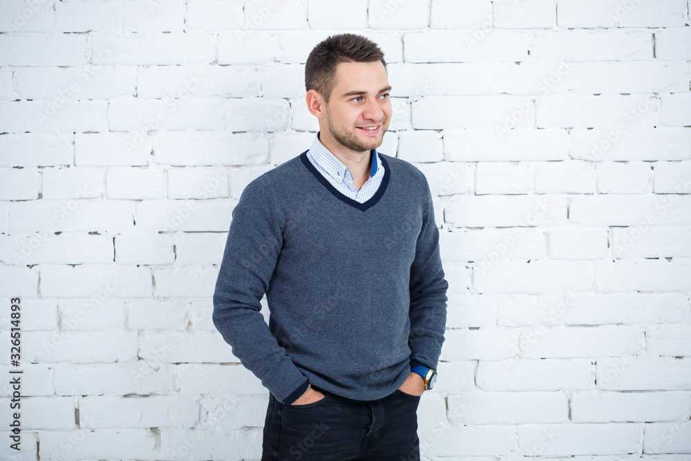 young guy in a shirt and sweater against a white brick wall young guy in a shirt and sweater against a white brick wall