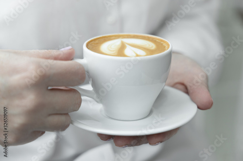 Woman hands holding cup of hot coffee latte cappuccino with with lush milk foam heart shaped.