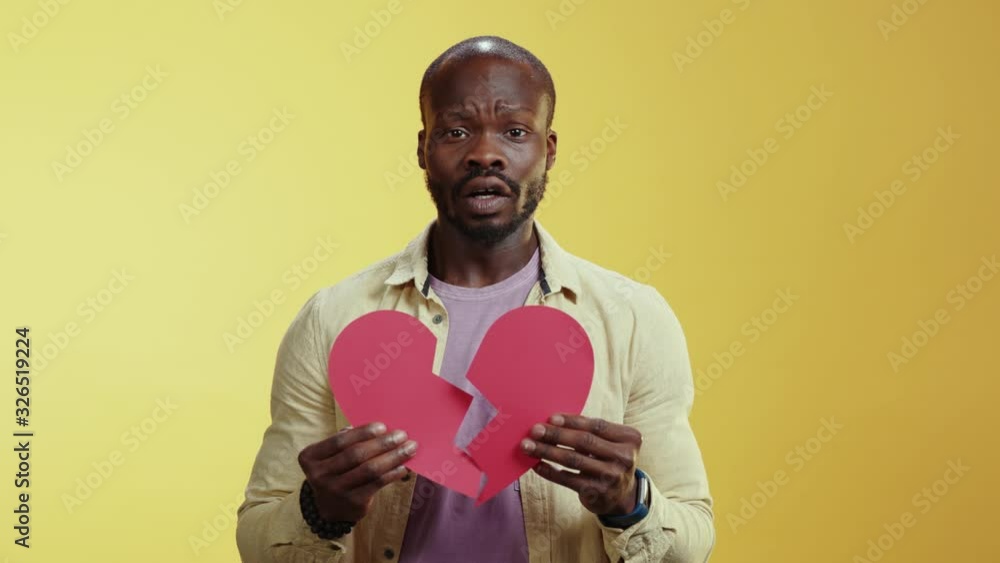 Romantic african man in love showing red paper heart celebrating Valentine's day. Unhappy man showing heartbreak expressing loneliness. Romantic african man in love showing red paper heart celebrating Valentine's day. Unhappy man showing heartbreak expressing loneliness.