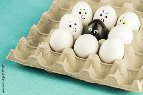 Black egg among angry, prejudiced white eggs attacking the black one. Xenophobic, racist concept. photo
