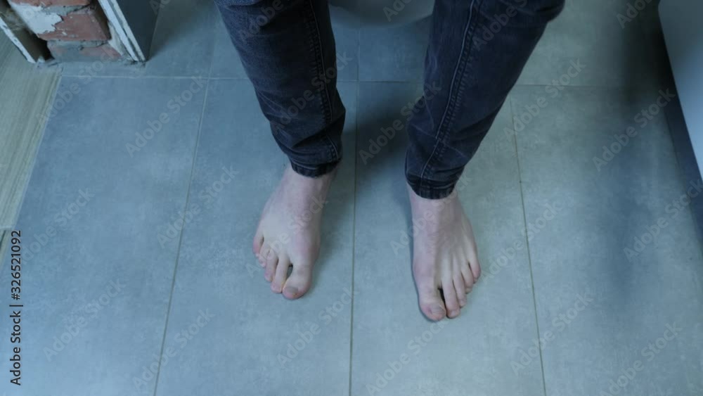 Man legs sitting on toilet. Male in jeans and bare feet sitting down on white toilet in bathroom