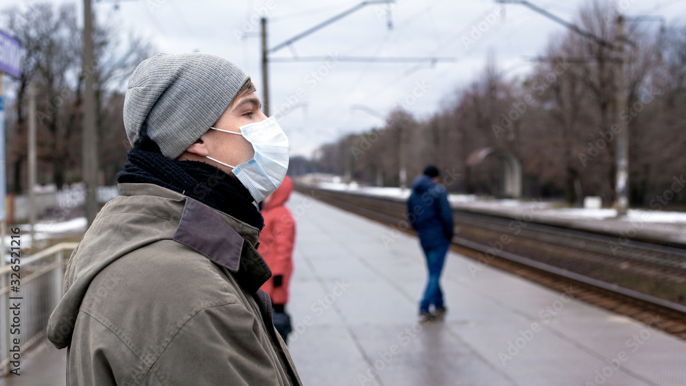 young guy in a medical disposable bandage on a crowded platform of the station. protection against respiratory bacterial and viral diseases