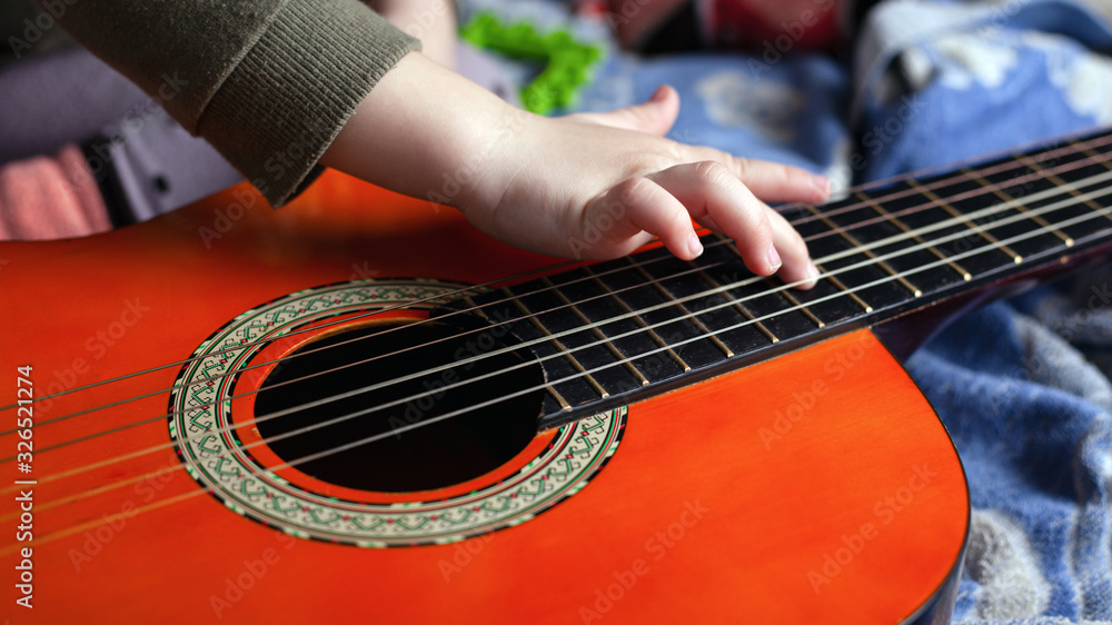 Fototapeta premium children's hand touches the strings on an acoustic six-string guitar. learning to play a musical instrument