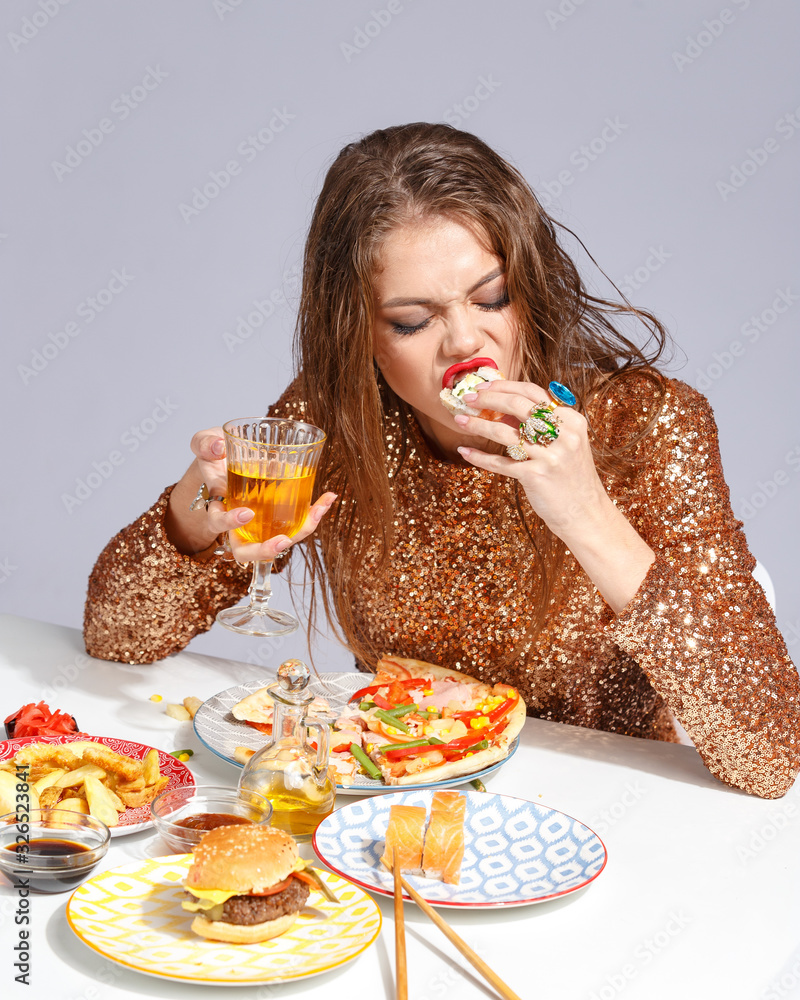 Beautiful young girl with bright makeup in an evening dress with an appetite eats fast food strength at the table. Creative fast food concept Beautiful young girl with bright makeup in an evening dress with an appetite eats fast food strength at the table. Creative fast food concept