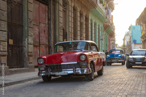 vintage red classic car on cobblestone street in front of old house in havana, cuba © Michael Barkmann