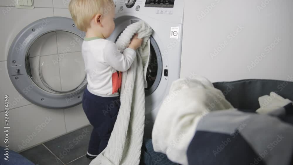 Two year old child doing household chores. Loading washing machine. Two year old child doing household chores. Loading washing machine.