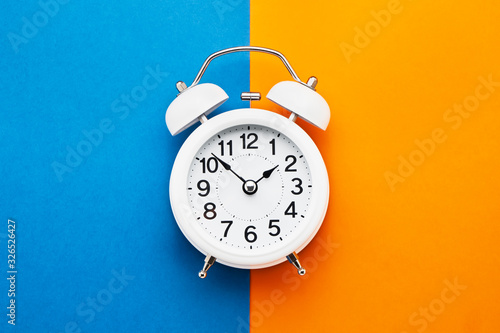 White vintage alarm clock on blue-orange background. Top view, copy space. Daylight saving concept. photo