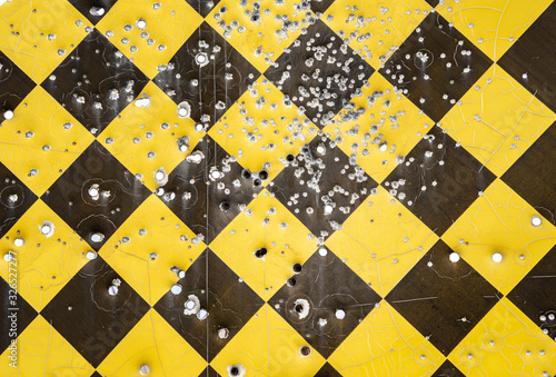 Close up of a yellow and black caution road sign full of bullet holes.