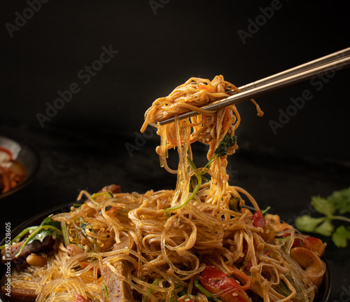 Chopsticks holdong Korean Japchae against black backround. Close up.