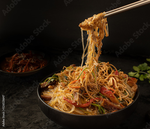 Chopsticks holdong Korean Japchae against black backround.