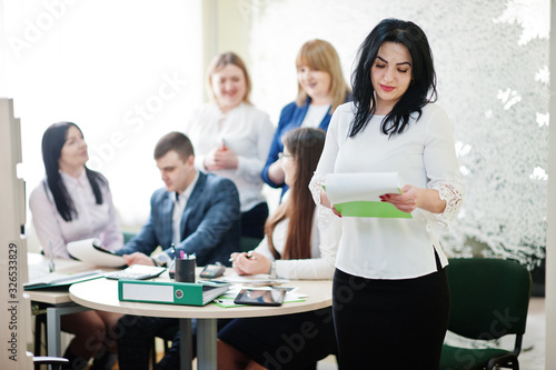 Portrait of caucasian woman in white blouse hold green folder against business people group of bank workers.