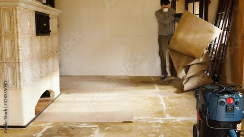 Time-lapse adult male worker wearing protective mask removing old dusty carpet in the empty house room during general renovation reconstruction