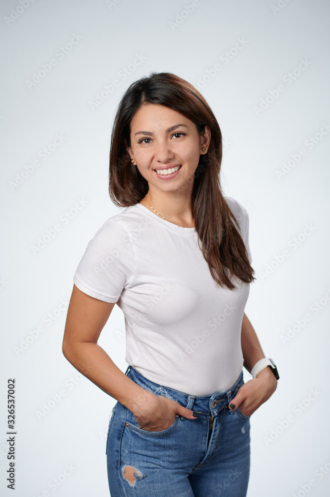 Smiling woman in white T-shirt standing with the hands in the pockets, white background Smiling woman in white T-shirt standing with the hands in the pockets, white background