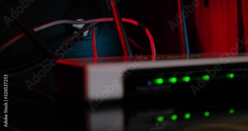 Home internet router on reflective surface with out of focus blinking green led lights, visible UTP cables and antenas, red light in the background. Close up shot.
