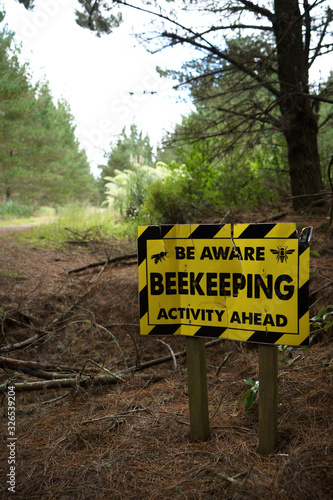 Be aware beekeeping activity ahead yellow and black sign warning sign beside an unpaved road track in Riverhead Forest, Kumeu, New Zealand. photo
