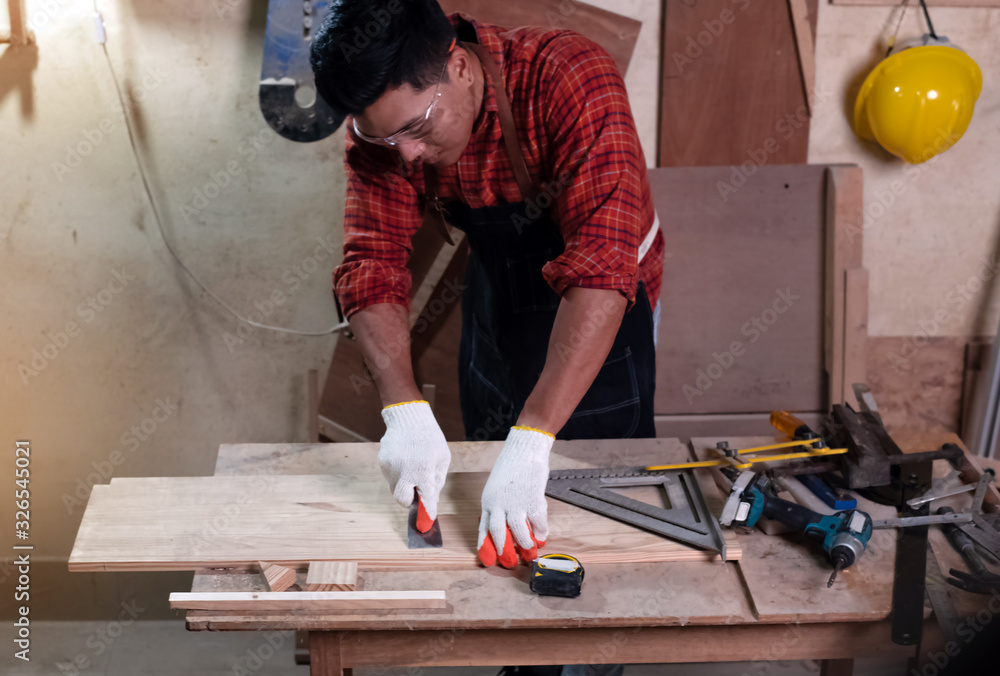 Handsome man wearing protective glasses and gloves,standing beside tools and equipment for doing wood work at factory,Handmade design,The carpenter