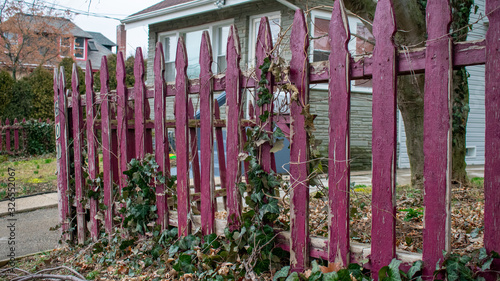 Fototapeta Naklejka Na Ścianę i Meble -  An OId Worn Red Wooden Fence With a House and a Tree in the Background