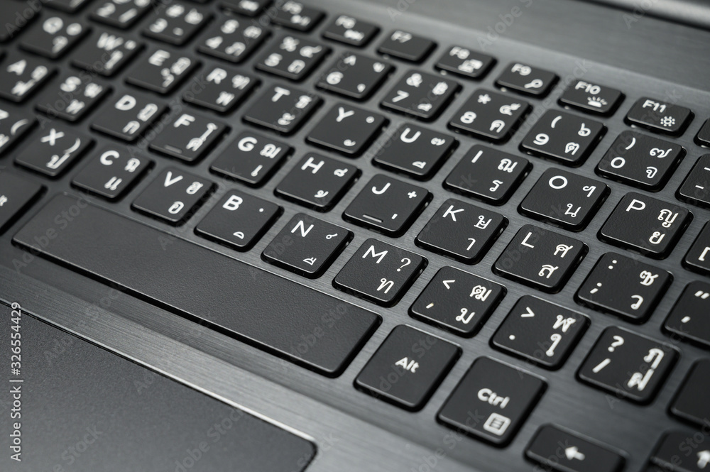 Black English-Thai keyboard and touchpad on metallic gray laptop (close-up) Black English-Thai keyboard and touchpad on metallic gray laptop (close-up)