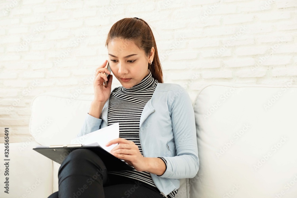 Beautiful Asian woman wearing striped shirt and blue jacket, working with the laptop on white sofa working on work desk at home Beautiful Asian woman wearing striped shirt and blue jacket, working with the laptop on white sofa working on work desk at home