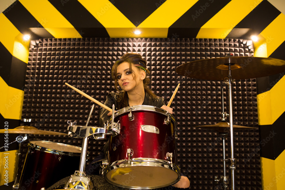 Fototapeta premium young beautiful tattooed girl in a leather jacket plays drums in a recording Studio on the bright black and yellow band