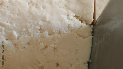 Closeup slicing raw tofu. Knife cuts through the white soybean curd for a plant based meal prep. Macro shot shows healthy vegan lifestyles and meat protein alternatives.