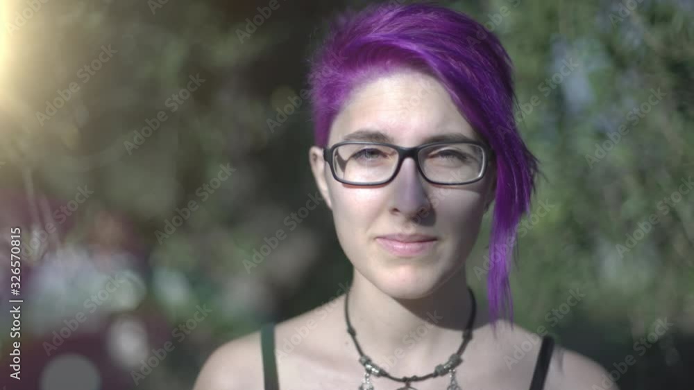 Beautiful portrait of attractive young modern woman with pink purple short hair and glasses in the park in summer or spring. Beautiful portrait of attractive young modern woman with pink purple short hair and glasses in the park in summer or spring.