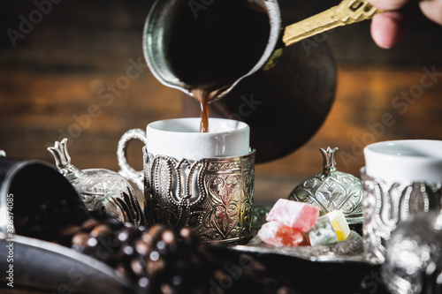 Pouring turkish coffee into vintage cup on wooden background with turkish delight