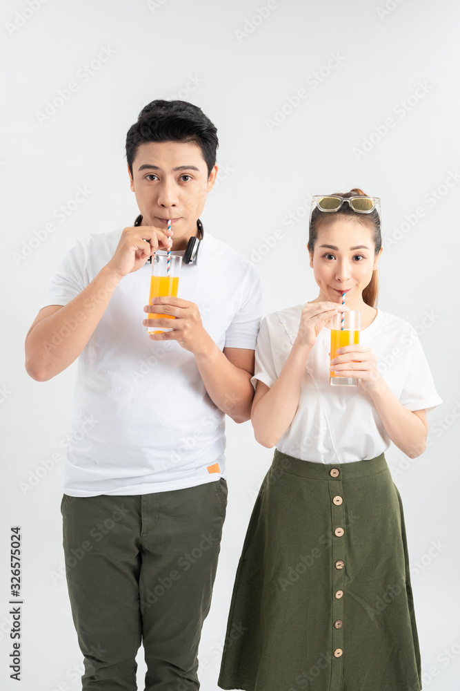Stylish couple in casual clothes is drinking juice, looking at camera and smiling on white background Stylish couple in casual clothes is drinking juice, looking at camera and smiling on white background