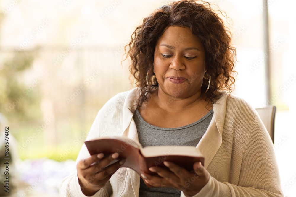 Mature African American woman sitting outside reading. - obrazy, fototapety, plakaty 