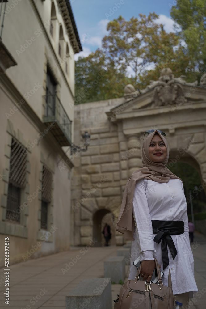 Asean young moslem woman wearing beige hijab stylish take a picture at the Colonnade in the courtyard of Charles V palace. Alhambra Site. Granada, Andalusia, Spain