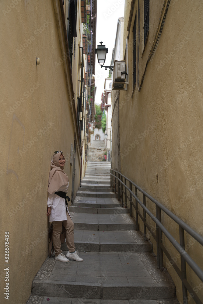 stylish moslem woman wearing white coat and beige scarf walking on the stair between the wall of the buildings