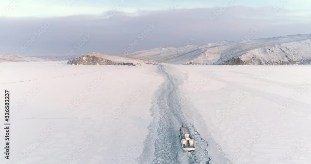 Drone Follow a Ship Icebreaker Moving on Ice. Beautiful Winter Landscape with Snow Covered Lake Baikal Surface. Travel Concept Drone Follow a Ship Icebreaker Moving on Ice. Beautiful Winter Landscape with Snow Covered Lake Baikal Surface. Travel Concept