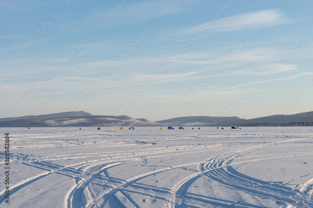 Φωτογραφία Traces of cars created patterns on the white snowy space of the frozen Big Lake